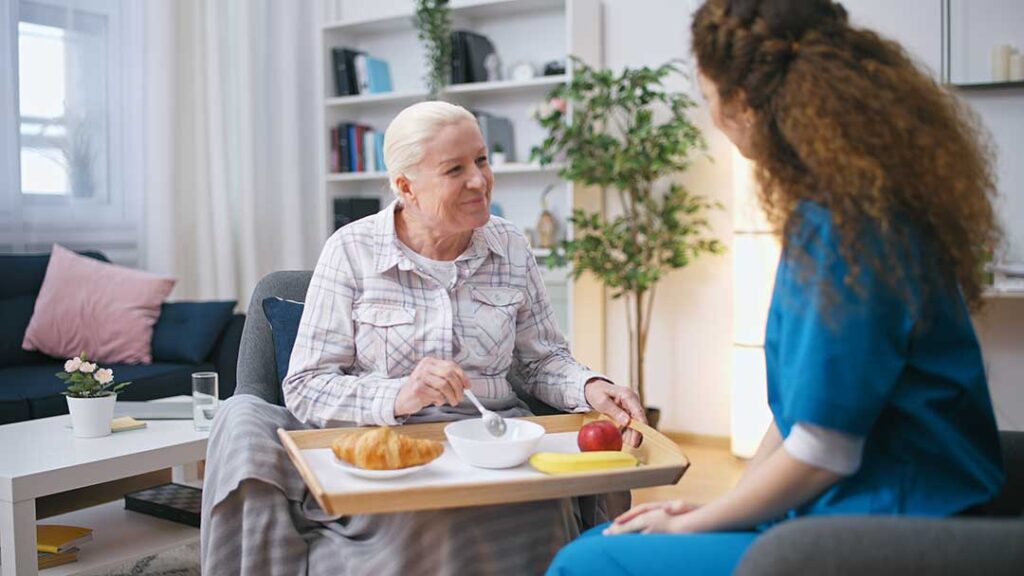 Older adults perform seated and standing exercises with resistance bands in a bright assisted living activity room.